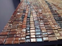 Close up of mosaic wall art featuring a wave pattern in amber, brick, and brown tones