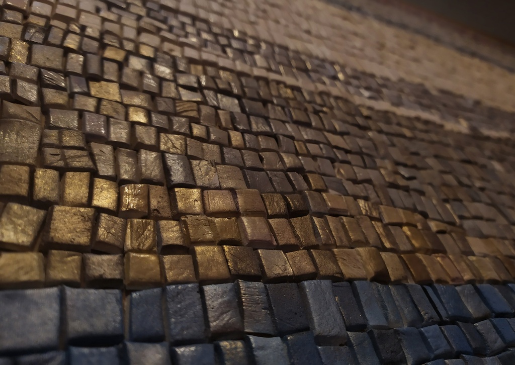 Detail of mosaic wall art with gold, navy blue, copper, and brown tiles